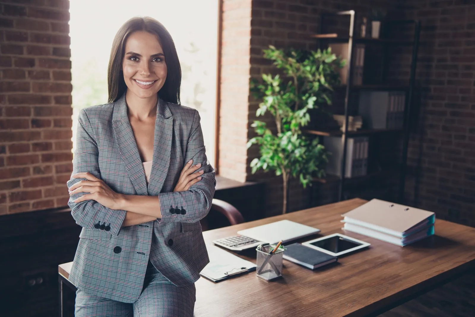 Smiling professional in a plaid blazer leaning on an office desk